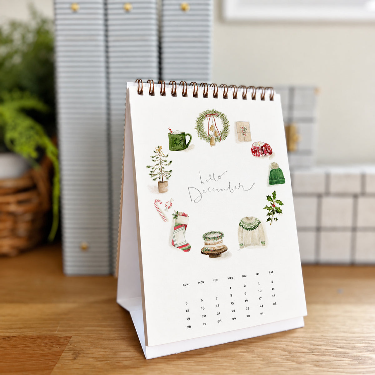 2027 hello month desk calendar December page with watercolor Christmas icons like a wreath, stocking, and sweater