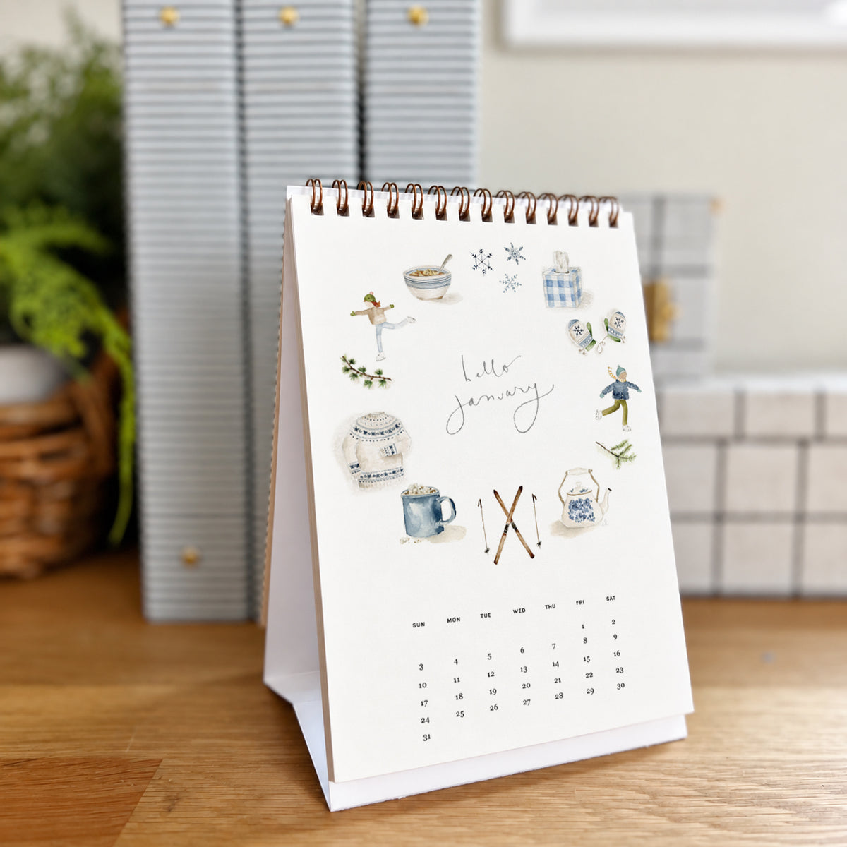 2027 hello month desk calendar January page with watercolor winter icons like a sweater, mug, mittens, and skis
