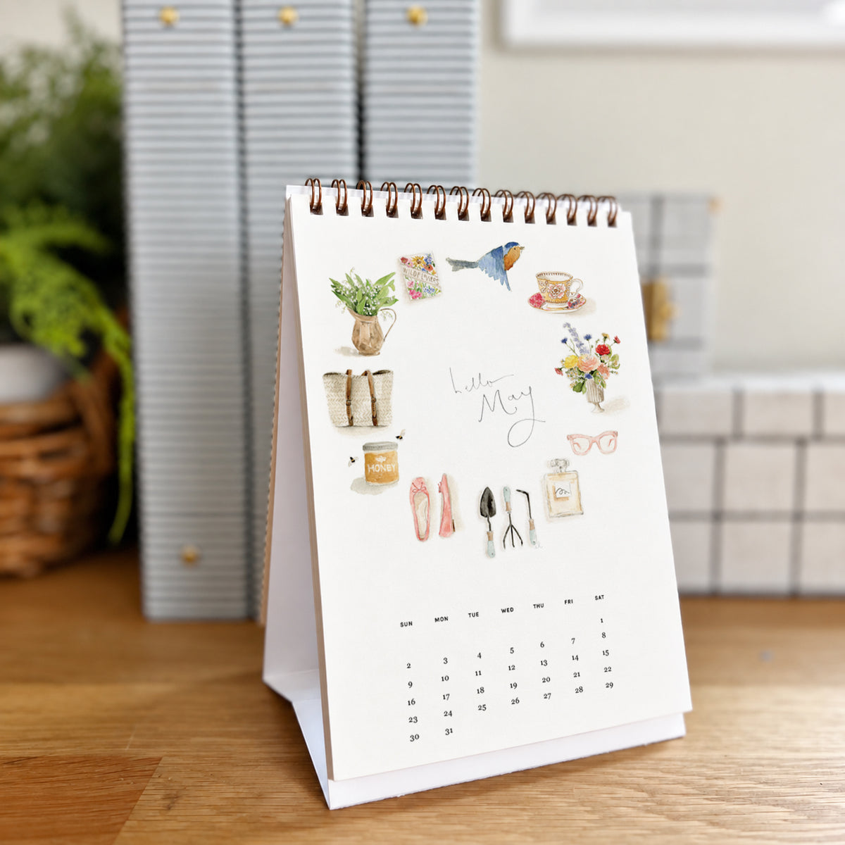 2027 hello month desk calendar May page with watercolor icons like a bird, teacup, ballet flats, and garden tools