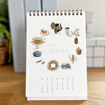 2027 hello month desk calendar November page with watercolor autumn icons like a turkey, pie, wreath, and acorn