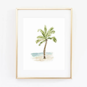 Palm tree watercolor wall art print of a single palm tree on a sandy beach by blue water, in a gold frame