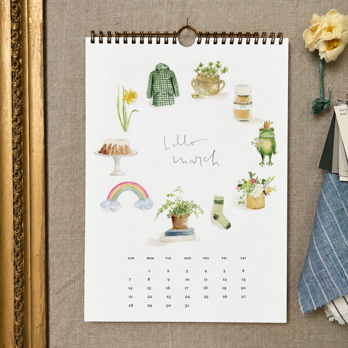 2027 hello month wall calendar March page with watercolor spring icons like a daffodil, rainbow, frog, and green coat