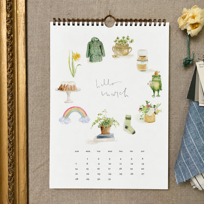 2027 hello month wall calendar March page with watercolor spring icons like a daffodil, rainbow, frog, and green coat